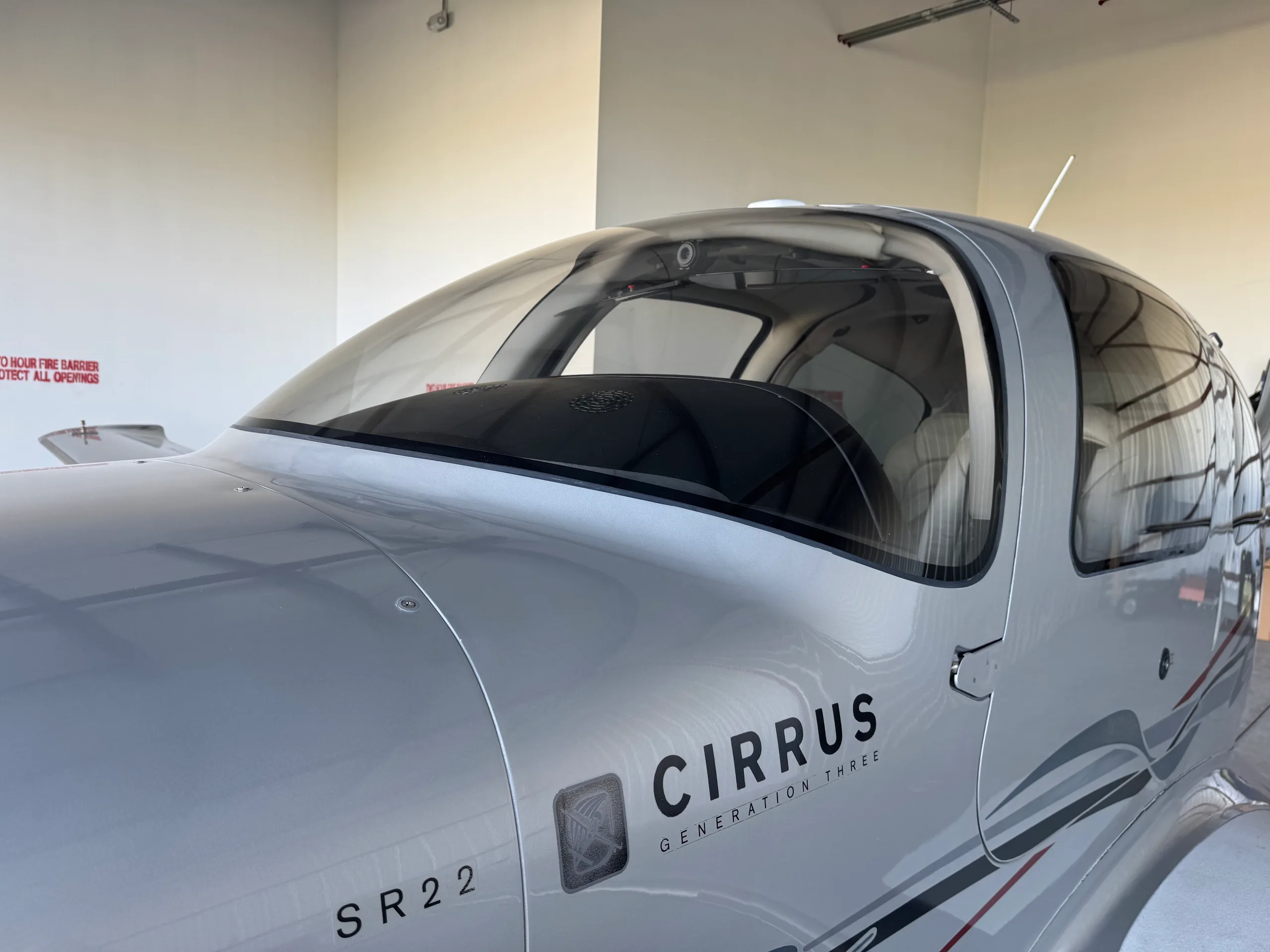 A close-up view of the nose and windshield of a silver Cirrus SR22 Generation Three aircraft, showing the "CIRRUS SR22 GENERATION THREE" text.