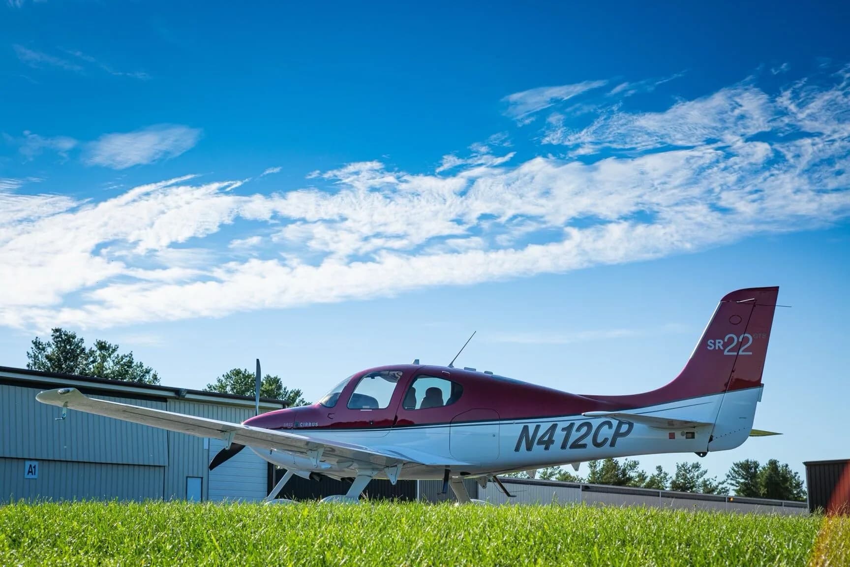 A red and white Cirrus SR22 aircraft (N412CP) parked on an airfield next to a hangar.