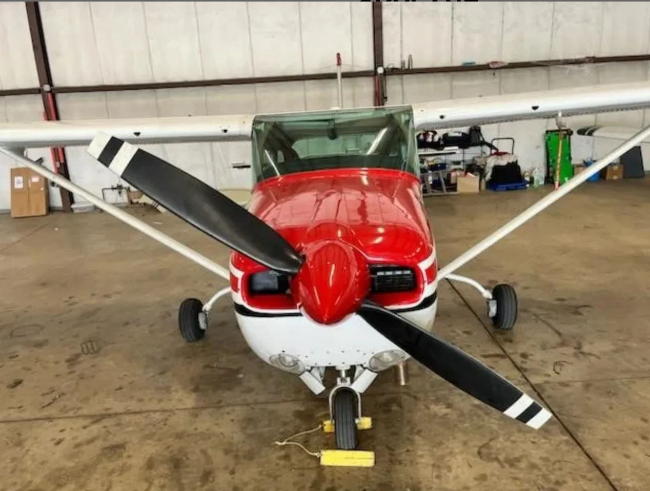 Front view of a red and white Cessna 182 Skylane with its propeller, parked inside a hangar.