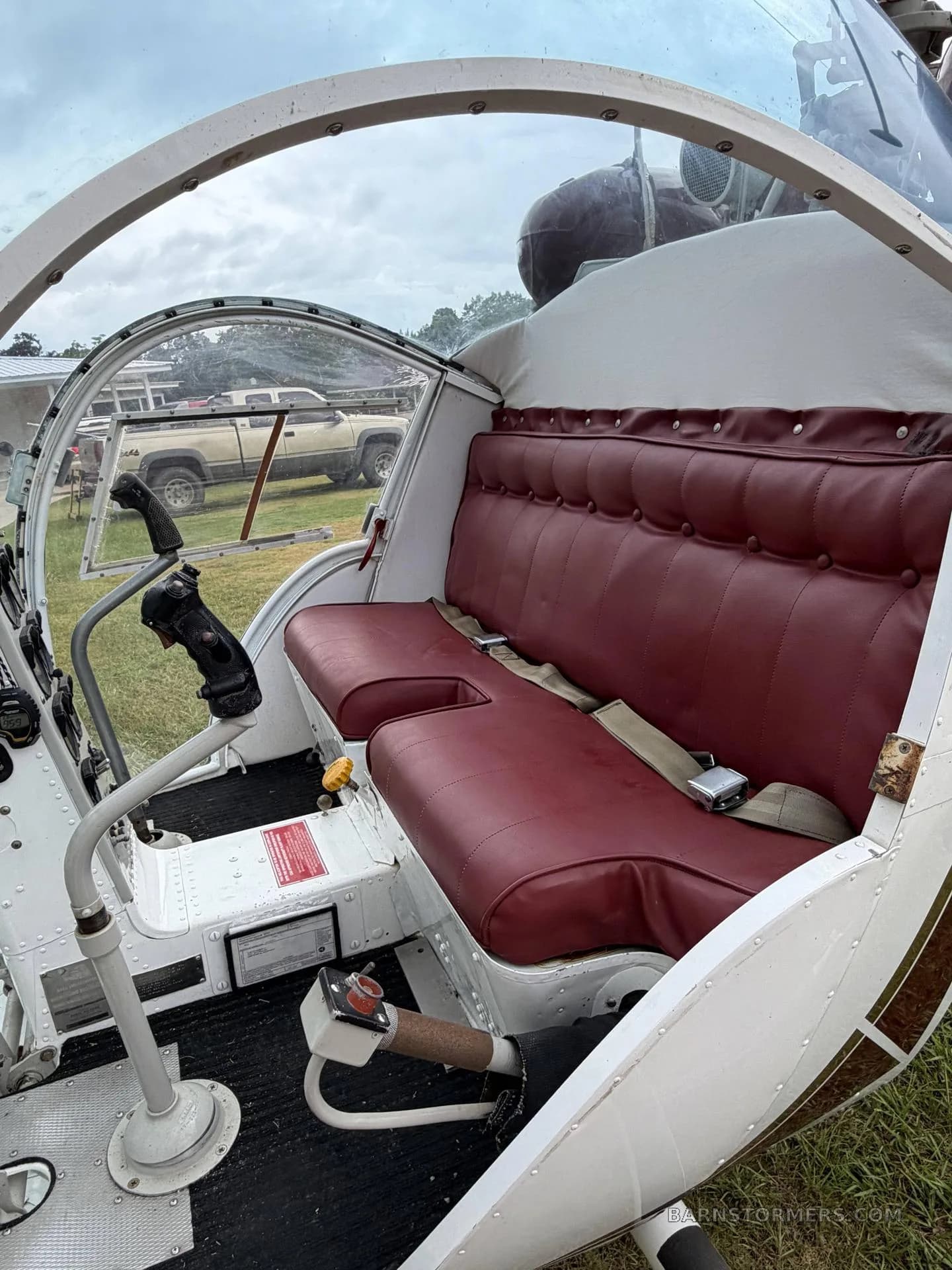 The interior of the helicopter showing red upholstered seats and basic flight controls.
