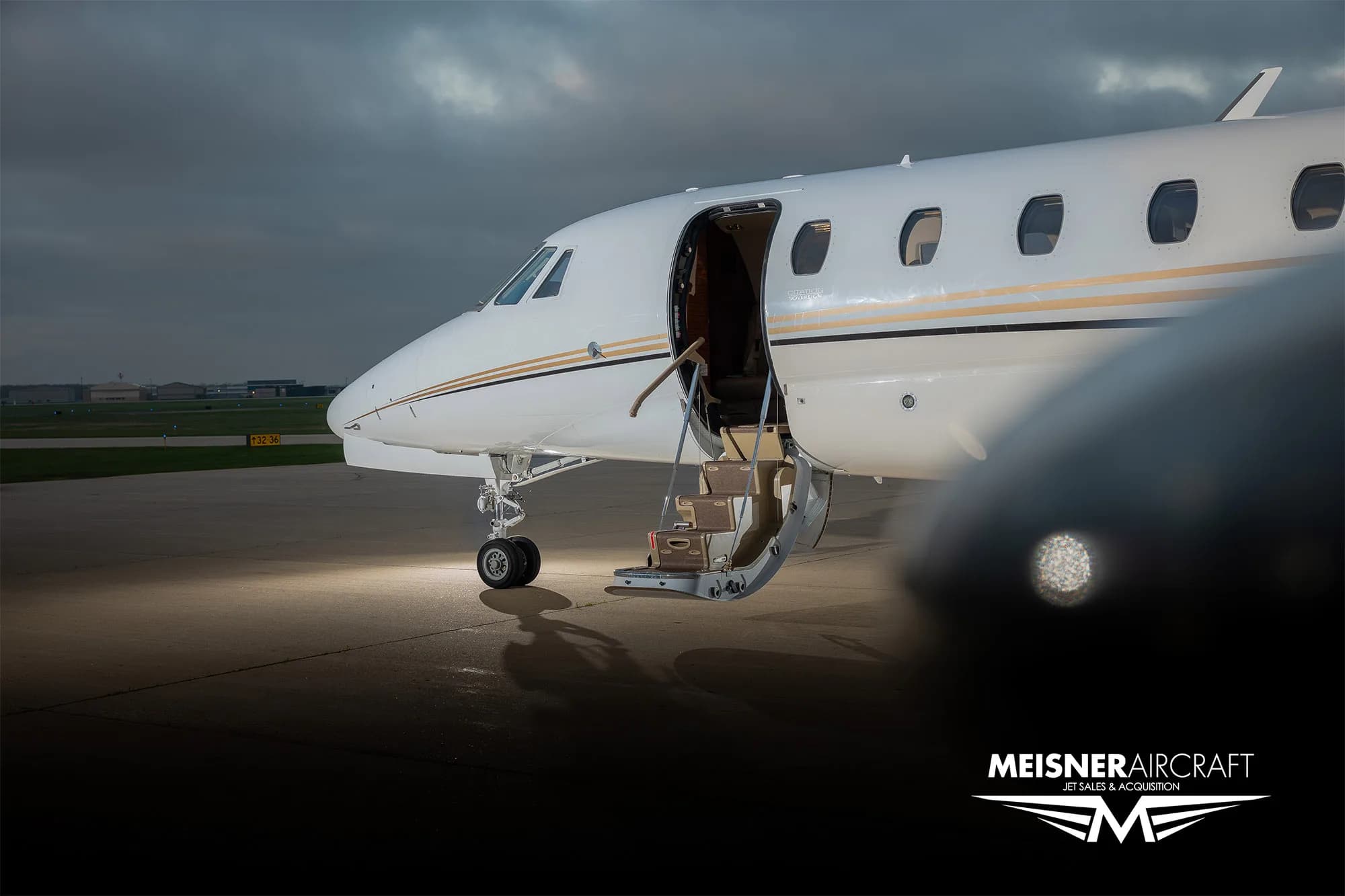 A close-up of the front fuselage of a white business jet with its entry door open and stairs deployed.