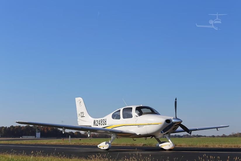 A Cirrus SR22 aircraft is parked on the tarmac on a sunny day.