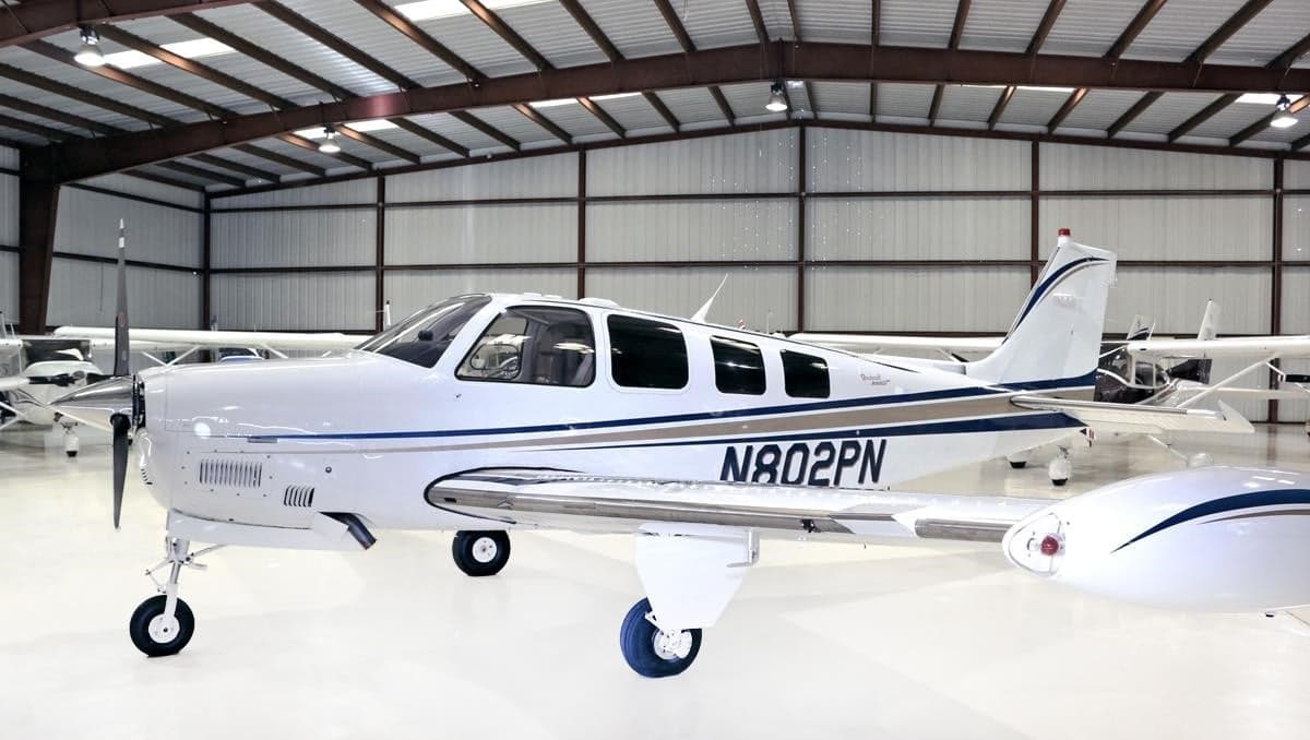 Side view of a white Beechcraft Bonanza N802PN with blue and grey stripes, parked in a hangar.