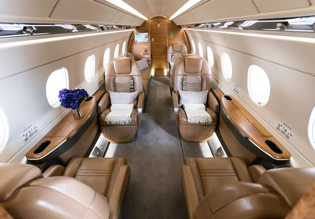 The luxurious interior cabin of a business jet features tan leather seats and wooden accents.