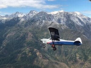 A Cubcrafters aircraft in flight over a mountainous landscape.