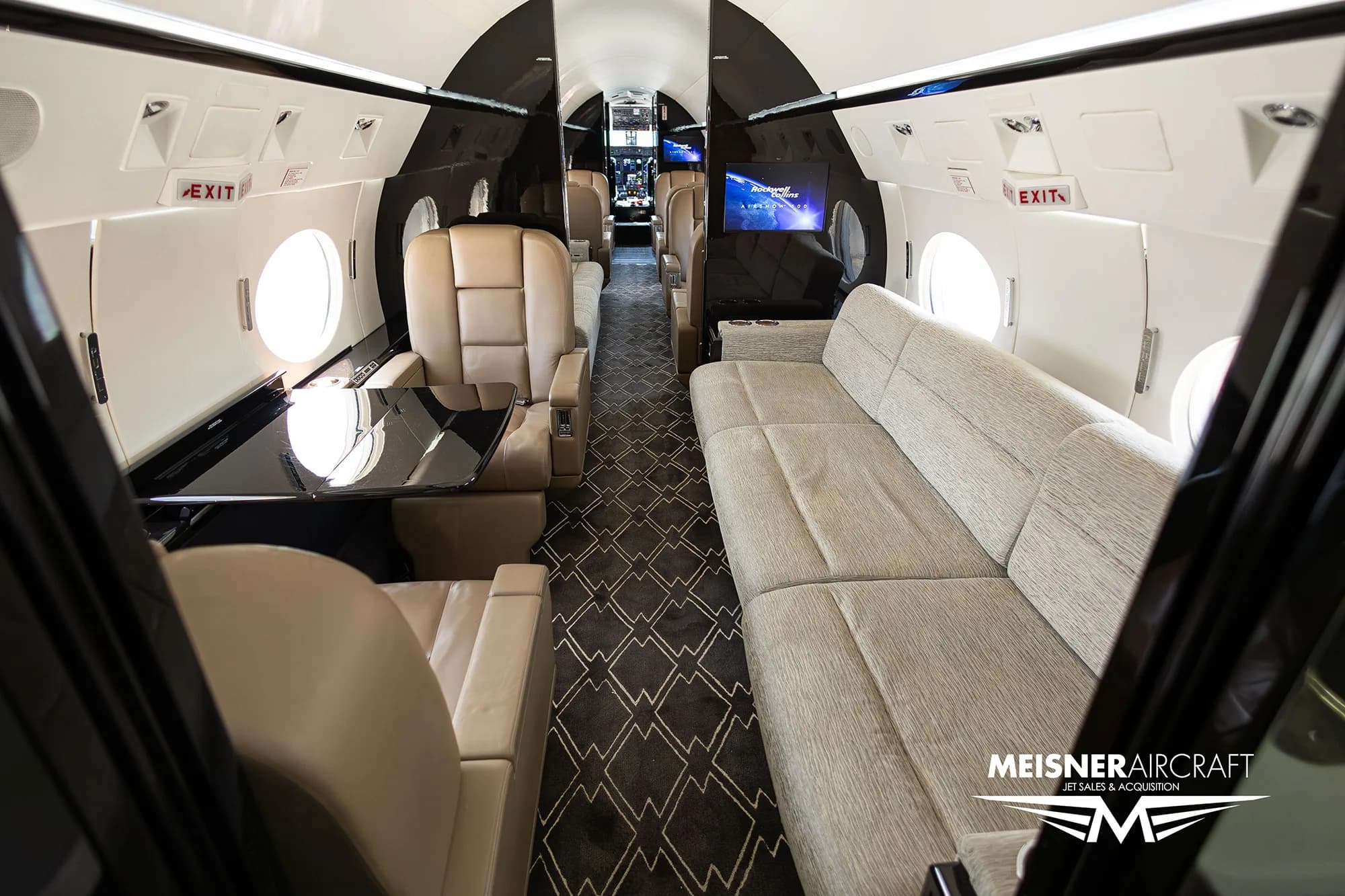 Aircraft cabin interior with a sofa, leather seats, and a table.