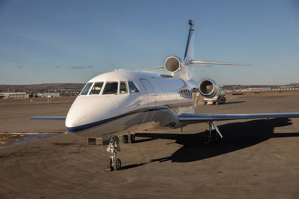A front-quarter view of a white and blue Dassault Falcon 900EX business jet parked on an airfield.