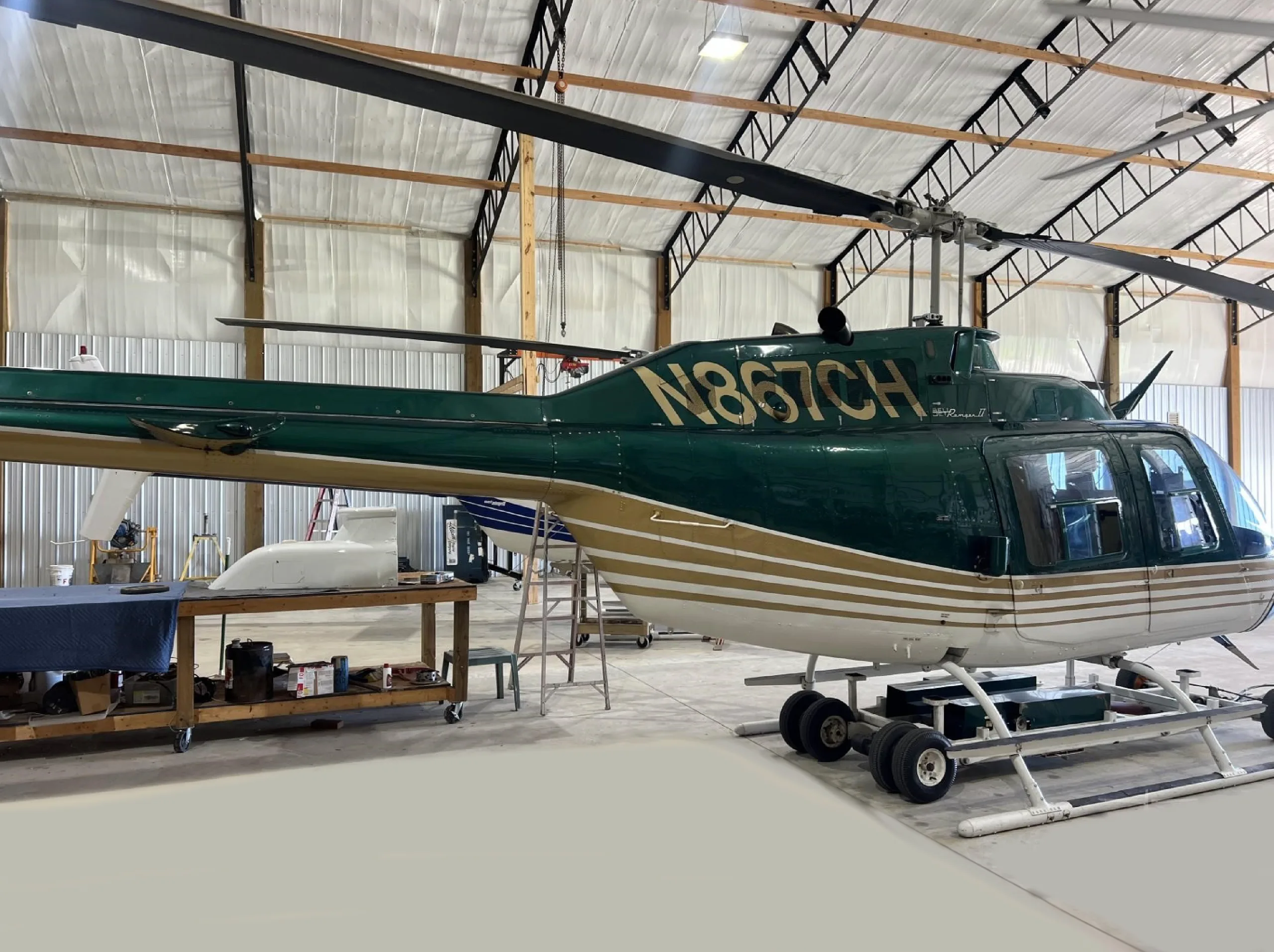 Side view of a green and white helicopter with registration N867CH in a hangar.
