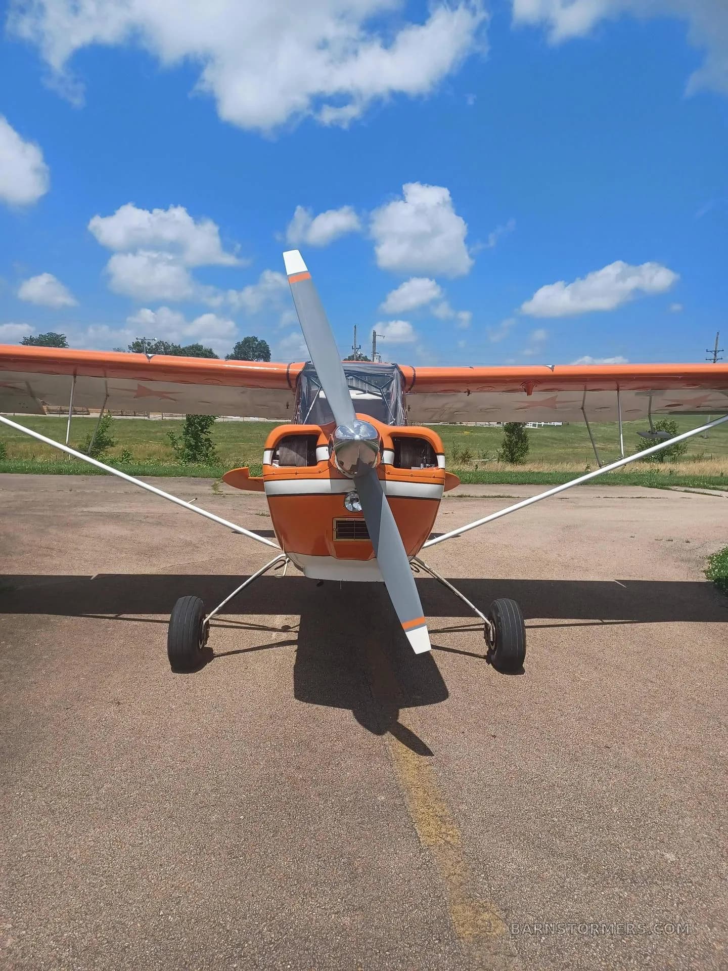 A head-on view of the orange and white aircraft, showing its propeller and front landing gear on a tarmac.