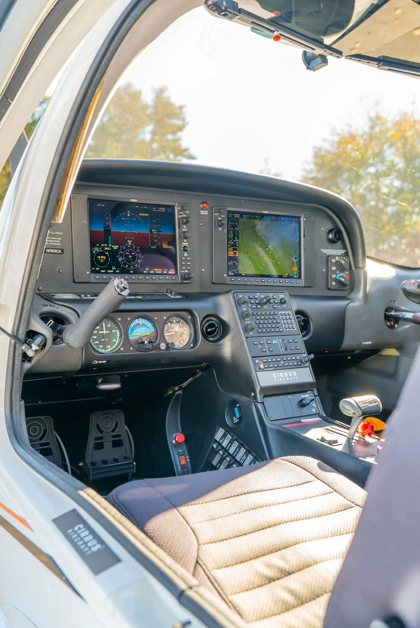 The cockpit of a Cirrus SR20 shows the instrument panel with two large digital displays and traditional gauges.