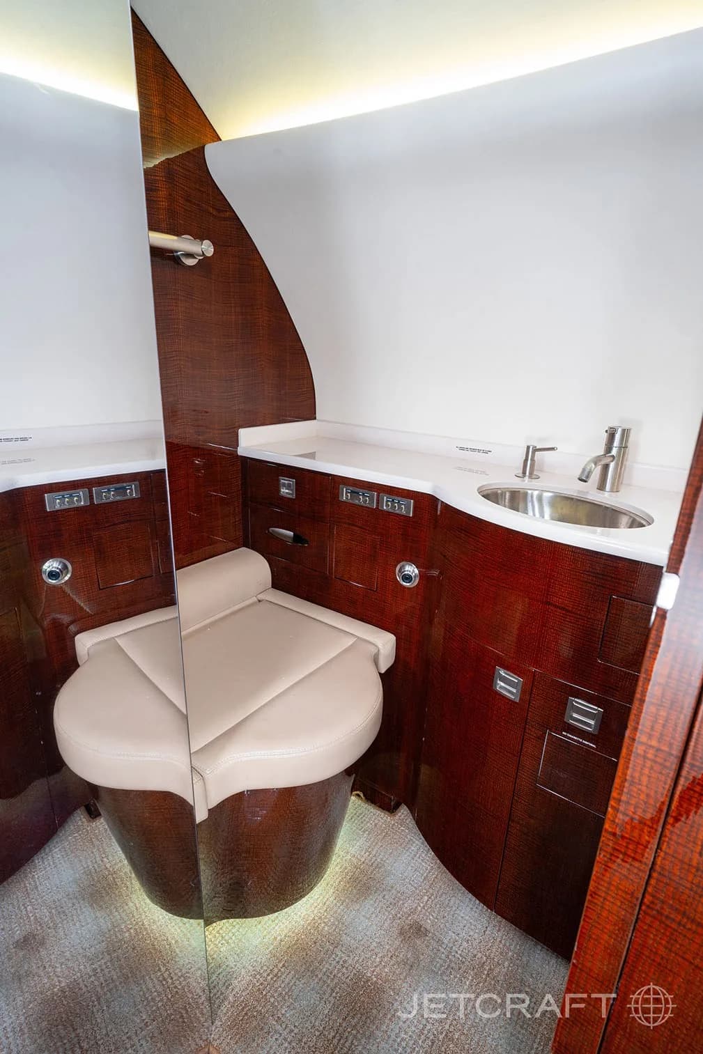 The aircraft lavatory featuring a beige toilet, a sink, and dark wood paneling.