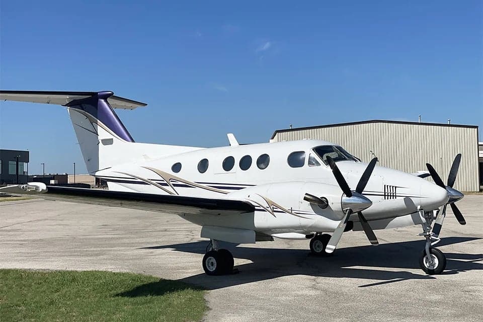A Beechcraft King Air is parked on the tarmac with a white and purple paint scheme.