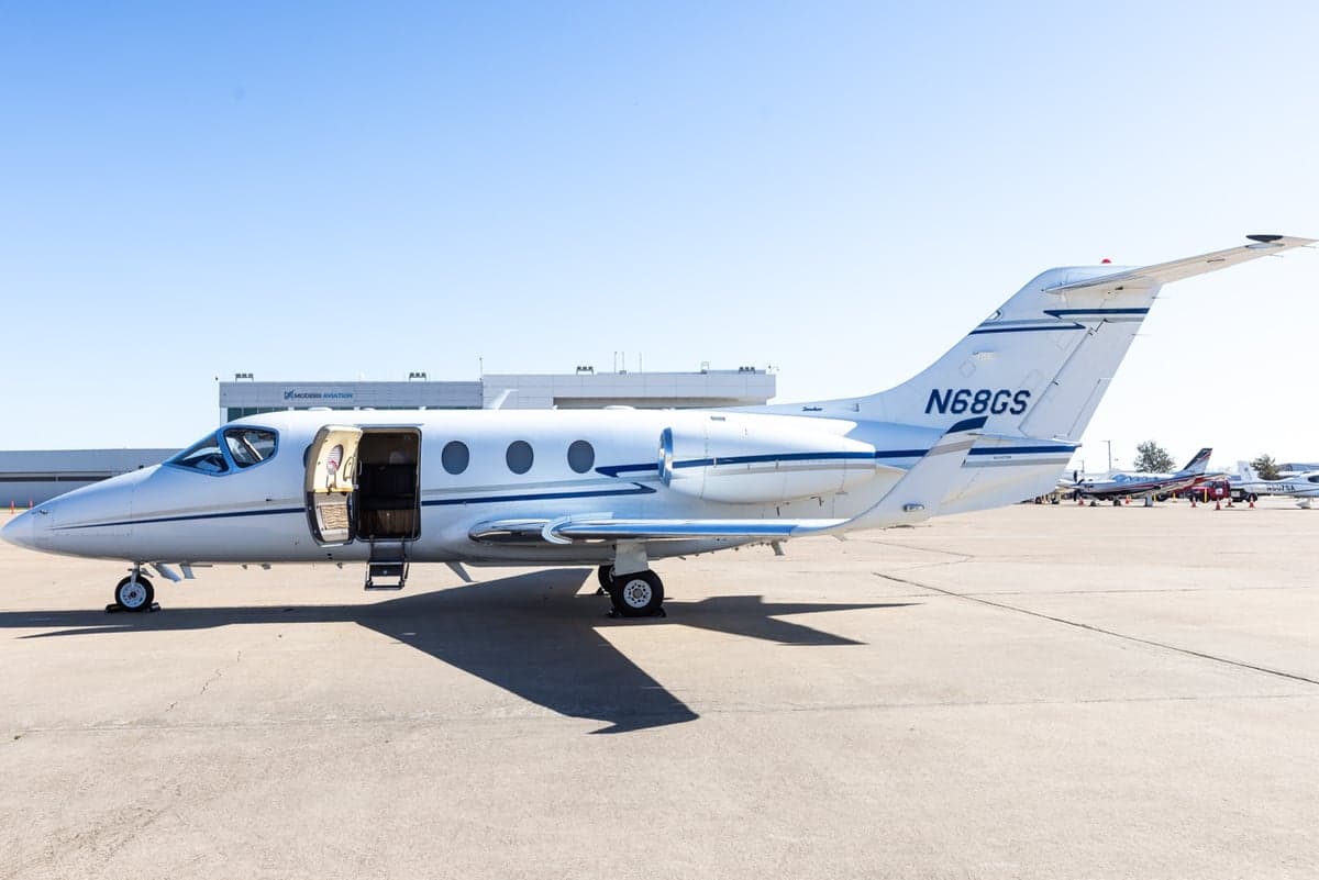 A white Learjet 45XR with blue stripes is parked on the tarmac with the door open.