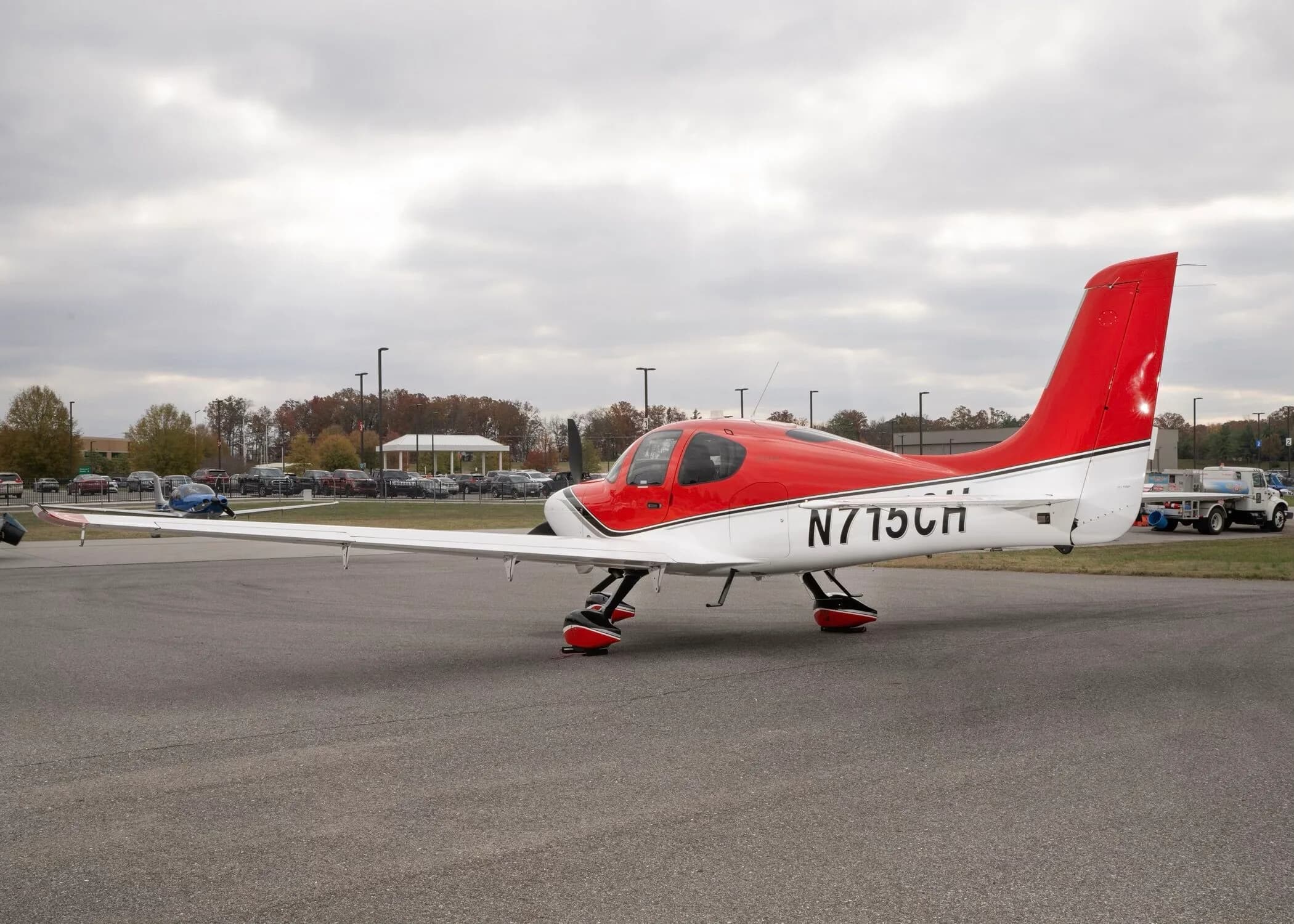 A red and white Cirrus SR22 aircraft with registration N715CH parked on an airfield under an overcast sky.