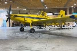Side view of a yellow and blue agricultural aircraft parked in a hangar.