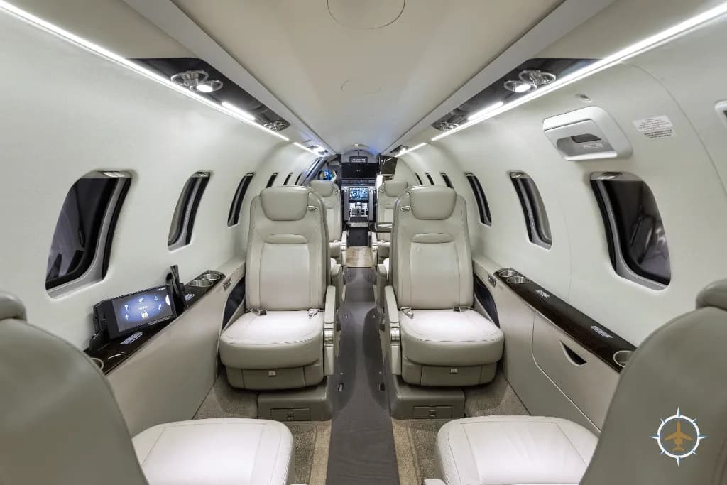 A wide view of a luxurious aircraft cabin with multiple rows of light-colored leather seats and screens on the side panels.
