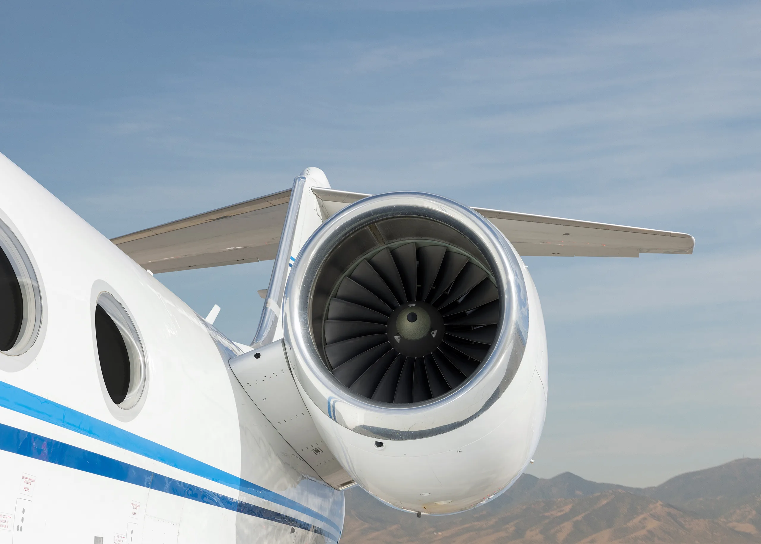 A close-up of a jet engine on the tail of a white business jet with a blue stripe.