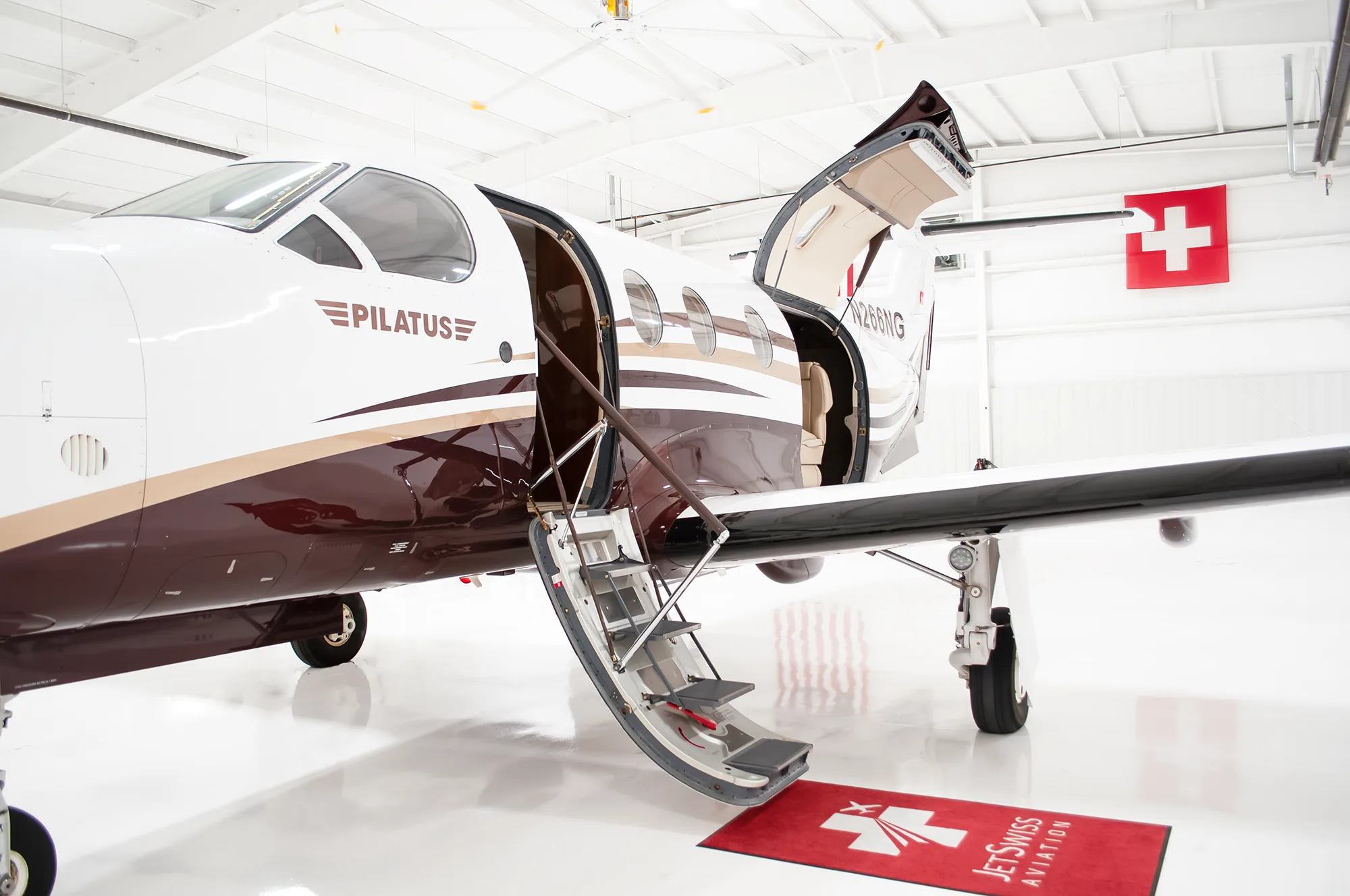 A Pilatus PC-12 NG aircraft, registration N266NG, with its main cabin door open and steps extended, parked in a hangar.