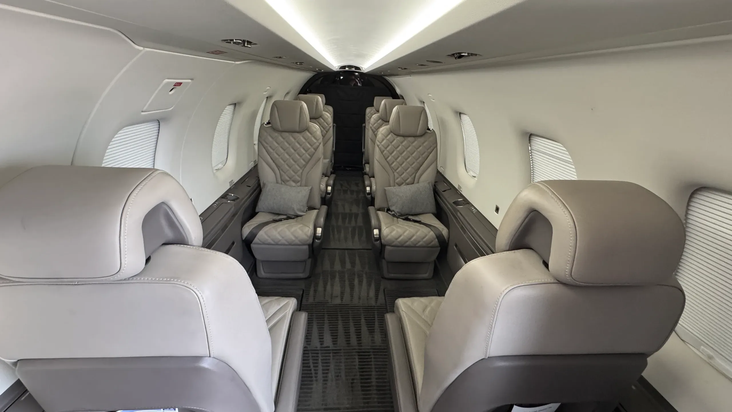 A view down the aisle of the Pilatus PC-12 cabin, showing light grey quilted seats and a bright ceiling.