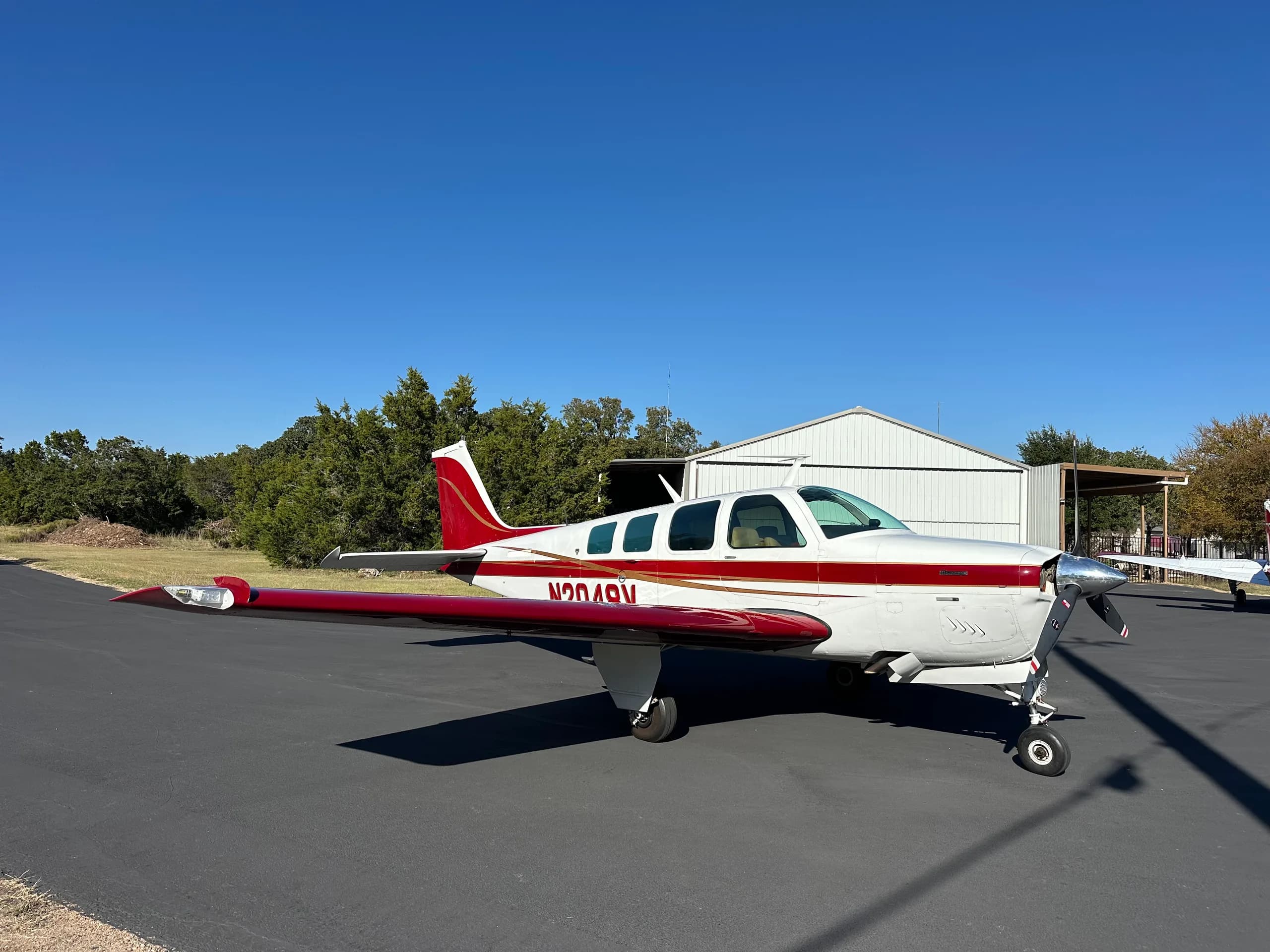 A Beechcraft Bonanza aircraft with a white and red paint scheme is parked on the tarmac.