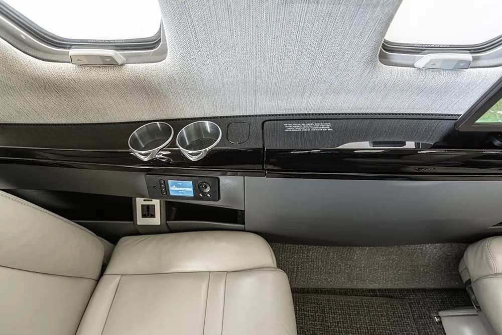 A detailed view of the private jet's cabin side panel, showing cup holders, a control panel, and a power outlet.