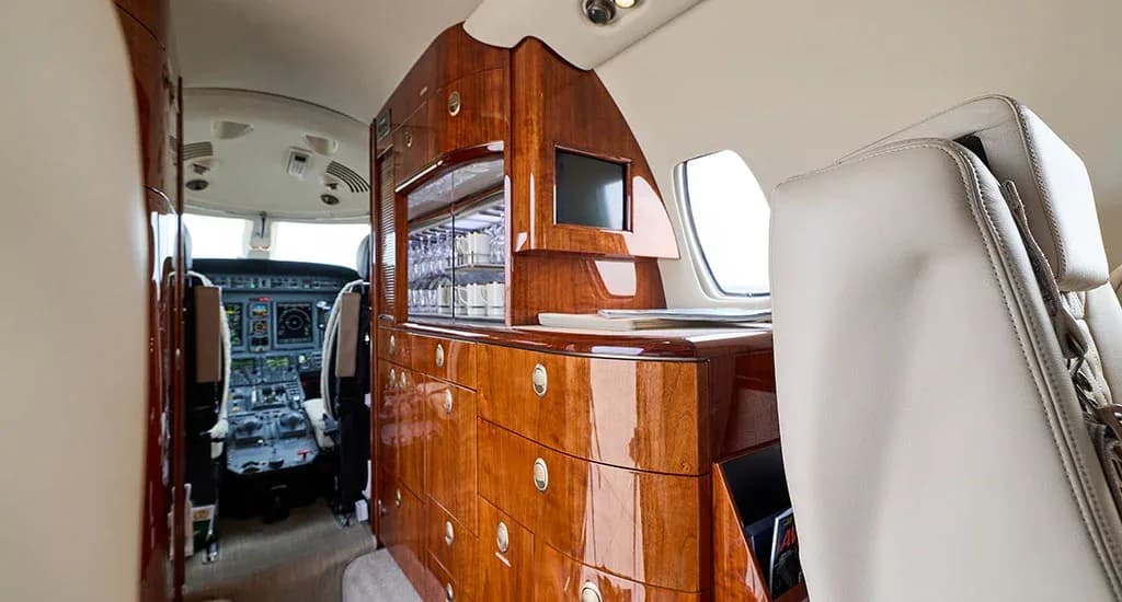 A close-up of the private jet's polished wood galley cabinetry, with the cockpit visible through the open door.