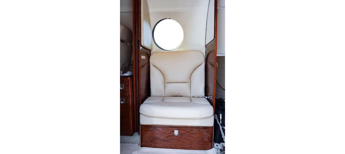 A single cream-colored leather seat inside the aircraft cabin with wood trim.