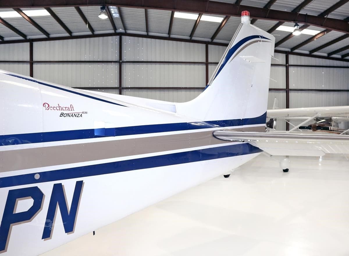 Close-up of the tail section of a white Beechcraft Bonanza N802PN with blue and grey stripes.