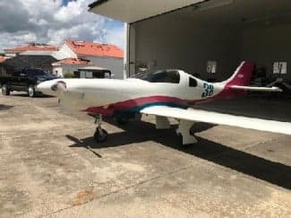 A white and pink aircraft with the number 38 on the side is parked in front of a hangar.