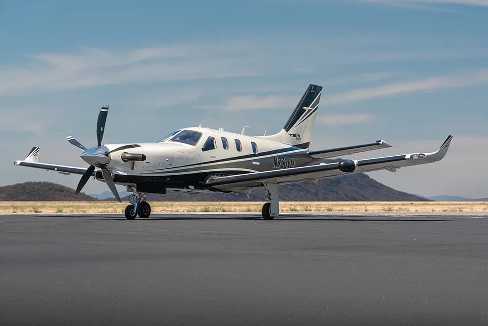 Side view of a white and black TBM 930 turboprop aircraft parked on an airfield.