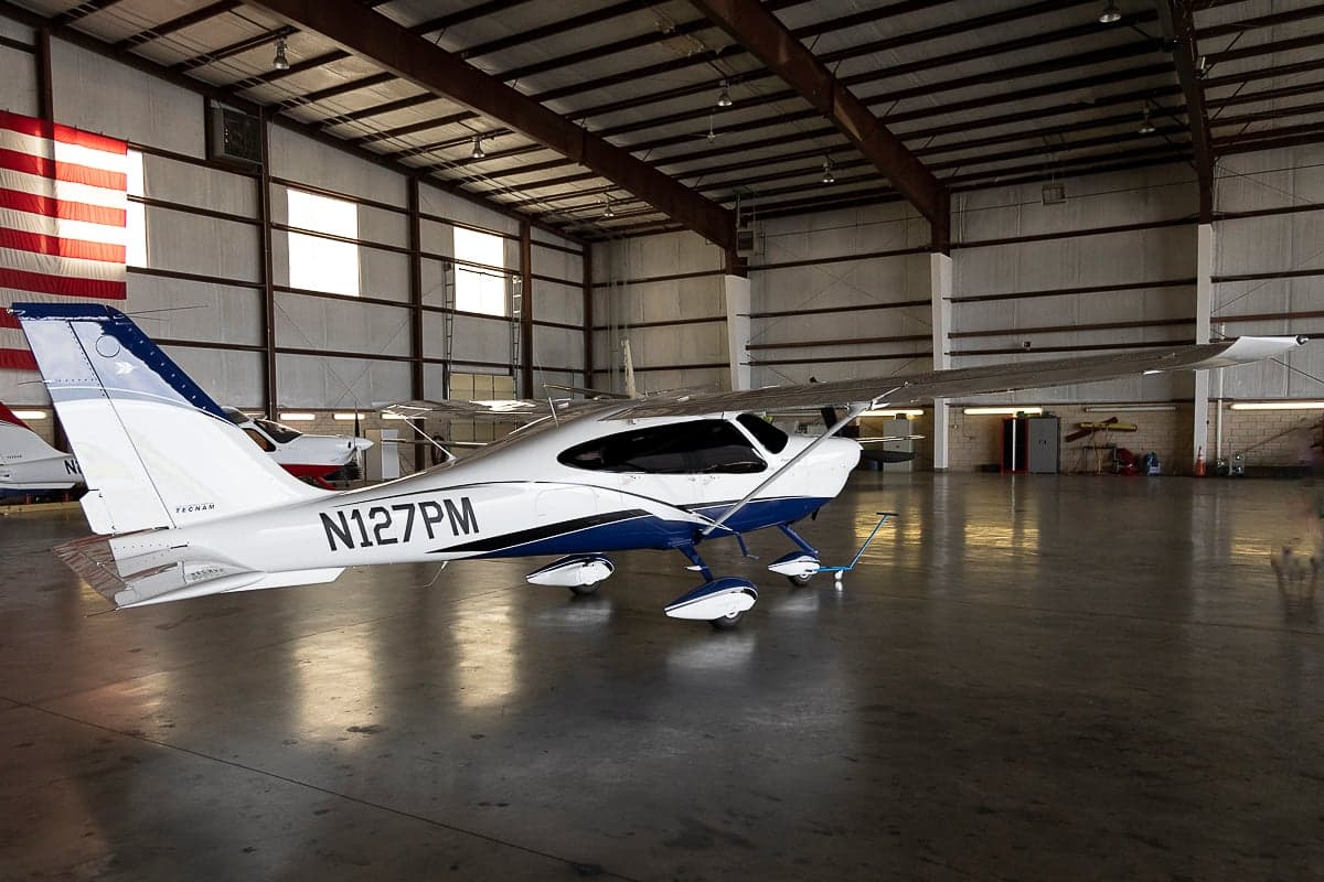 Tecnam P2010 aircraft with blue and white paint scheme in a hangar.