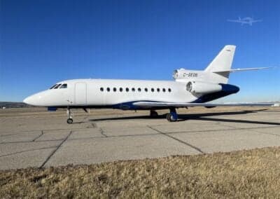 A white and blue Dassault Falcon 900EX, registration C-GEOS, parked on the tarmac.