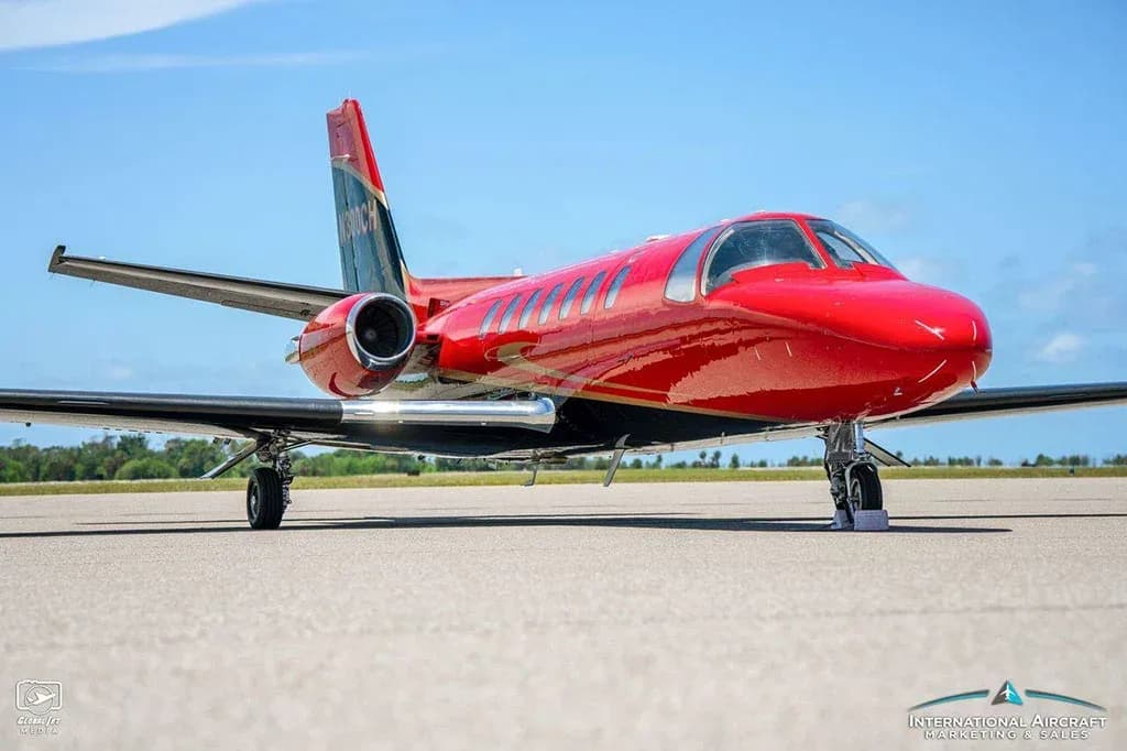 A three-quarter front view of the red and black Cessna Citation V jet on a tarmac under a blue sky.