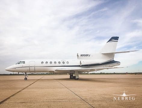A white business jet with a dark blue stripe, registration N950FJ, parked on an airport tarmac under a cloudy sky.