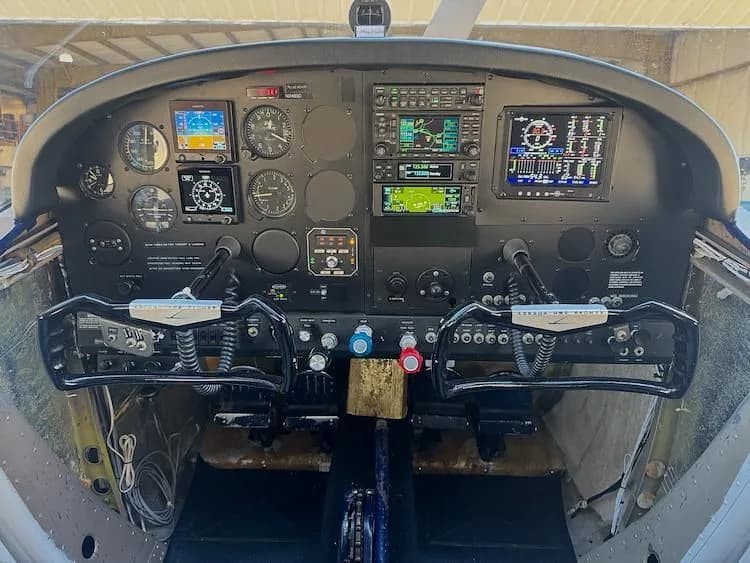 The cockpit of a Cessna 180 Skywagon, featuring a modern avionics panel with multiple digital displays and traditional yokes.