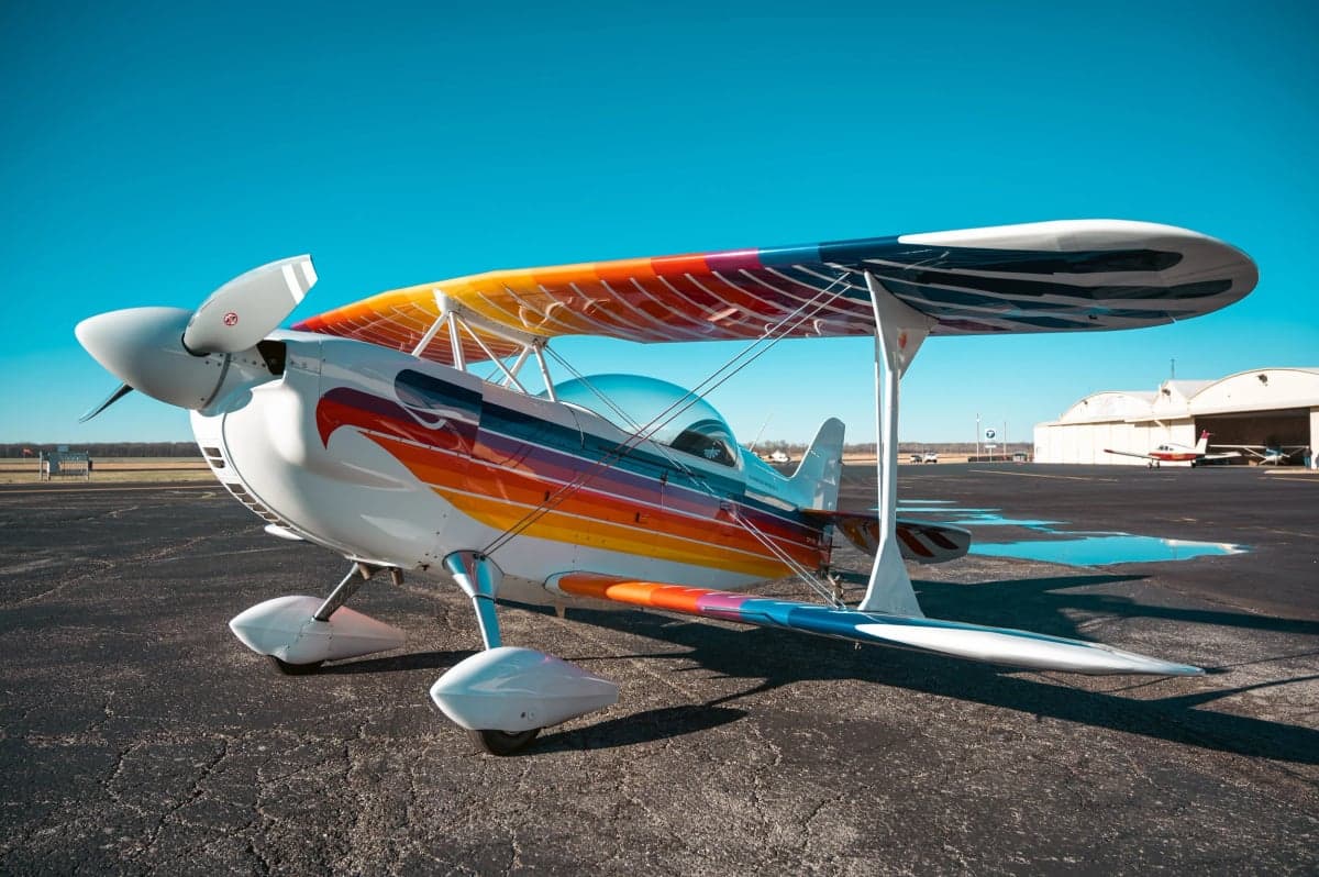 Christen Eagle II biplane with a colorful paint scheme parked on the tarmac in front of a hangar.