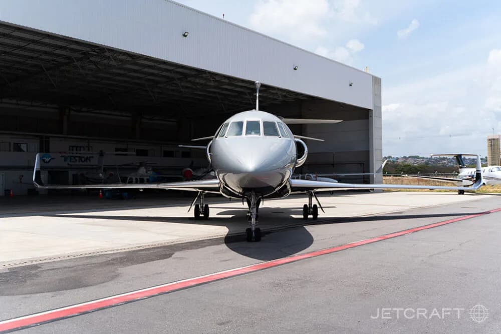 A silver and black business jet parked head-on in front of an open hangar on a sunny day.