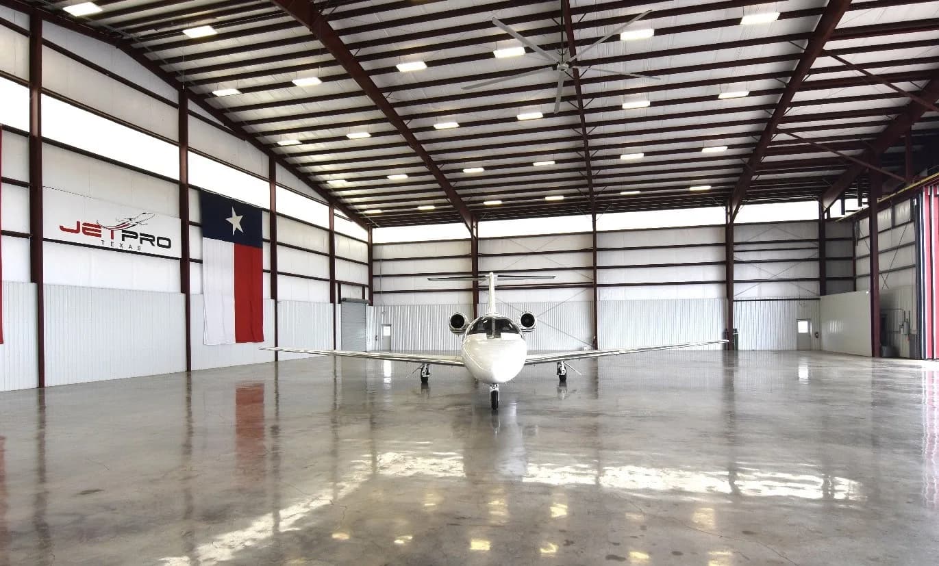 A white Cessna Citation CJ3 private jet, registration N525TK, viewed from the front in a hangar with a Texas flag.