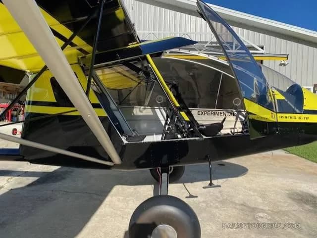 A close-up side view of the black and yellow ultralight aircraft with its canopy open, revealing the "EXPERIMENTAL" label.