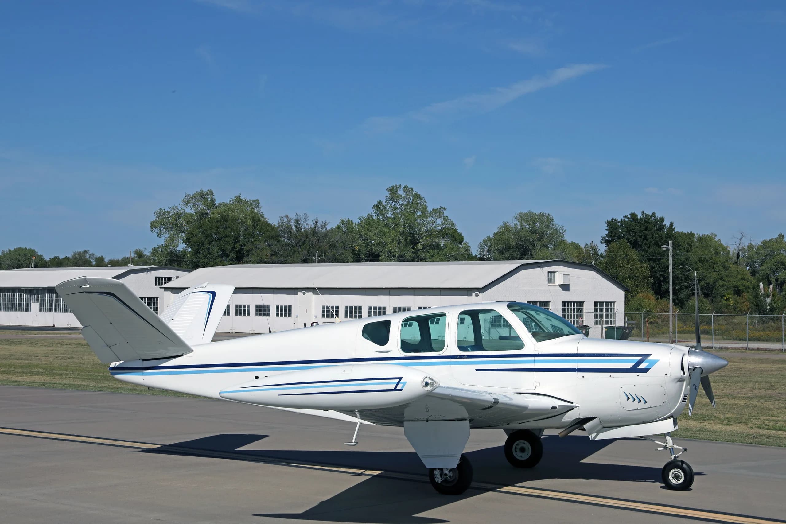 A side view of a white single-engine aircraft with blue stripes, registration N4696D, parked on an airfield.
