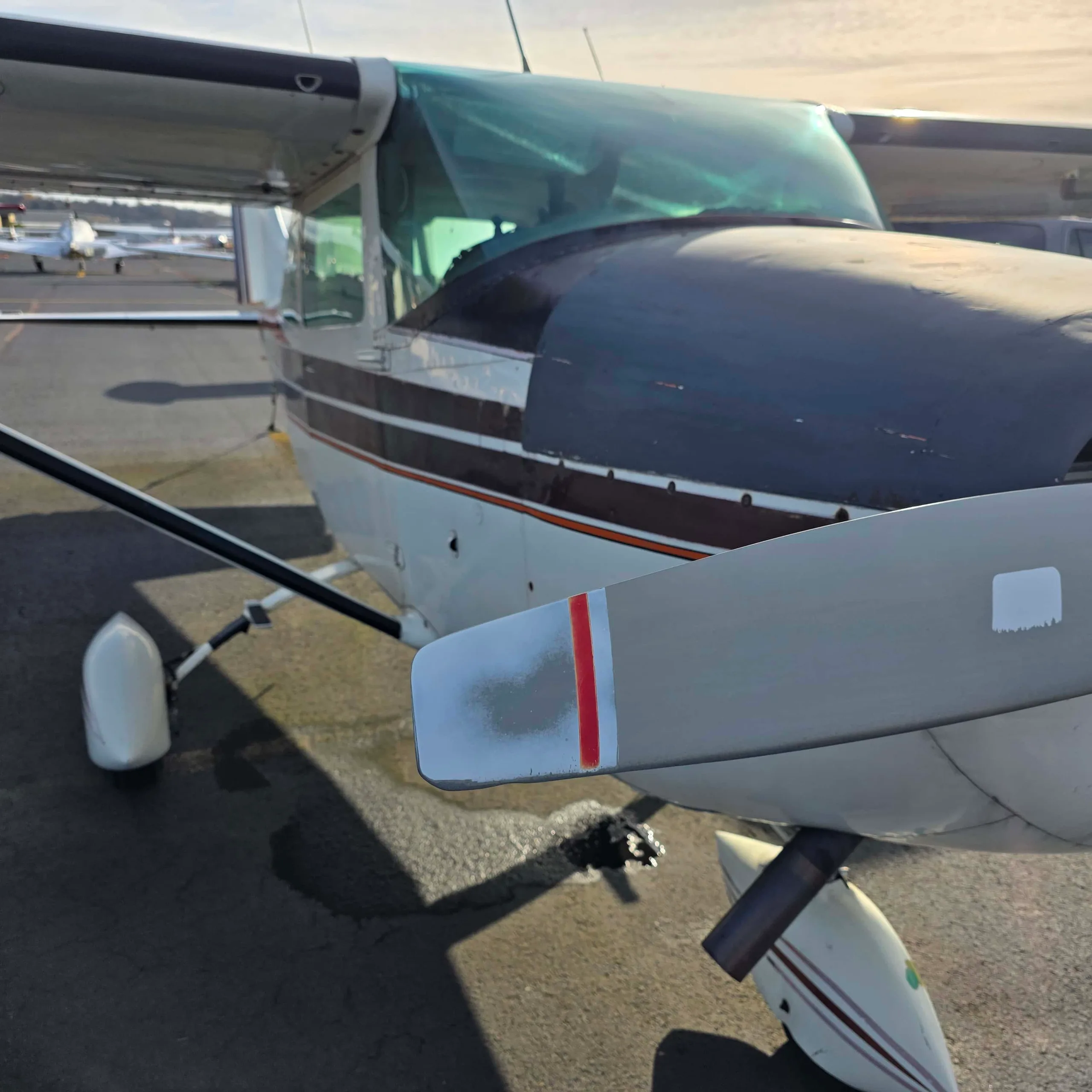 A close-up, front-right view of a white and dark-striped high-wing aircraft with a propeller, parked on an airfield.
