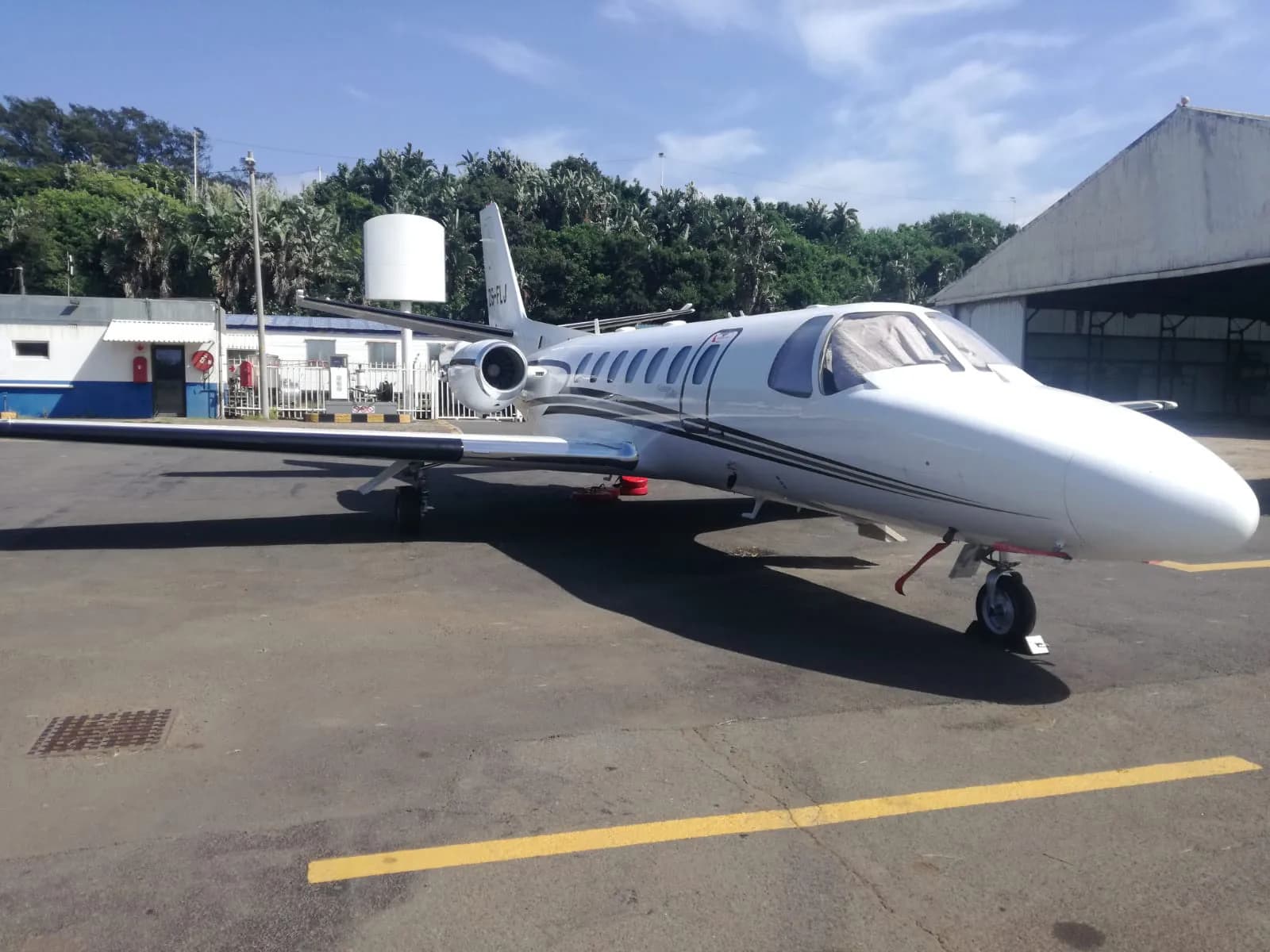 A white business jet with black accents, possibly a Cessna Citation, parked on an airport tarmac next to a hangar.