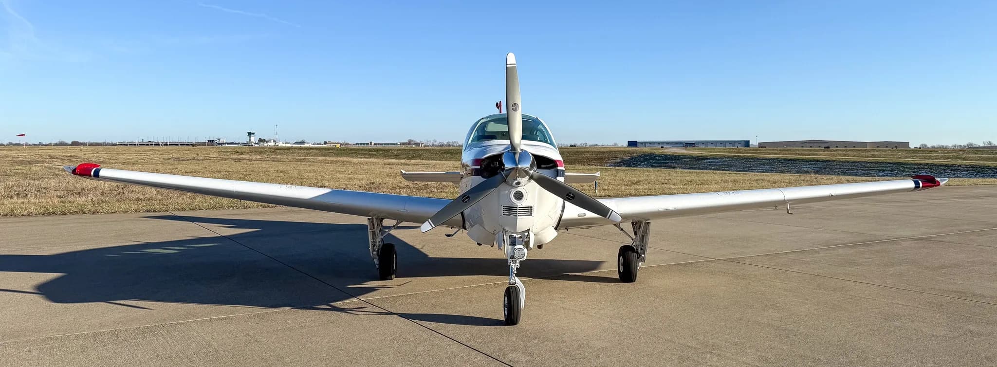 Front view of a white Beechcraft Bonanza with a single propeller on an airfield.