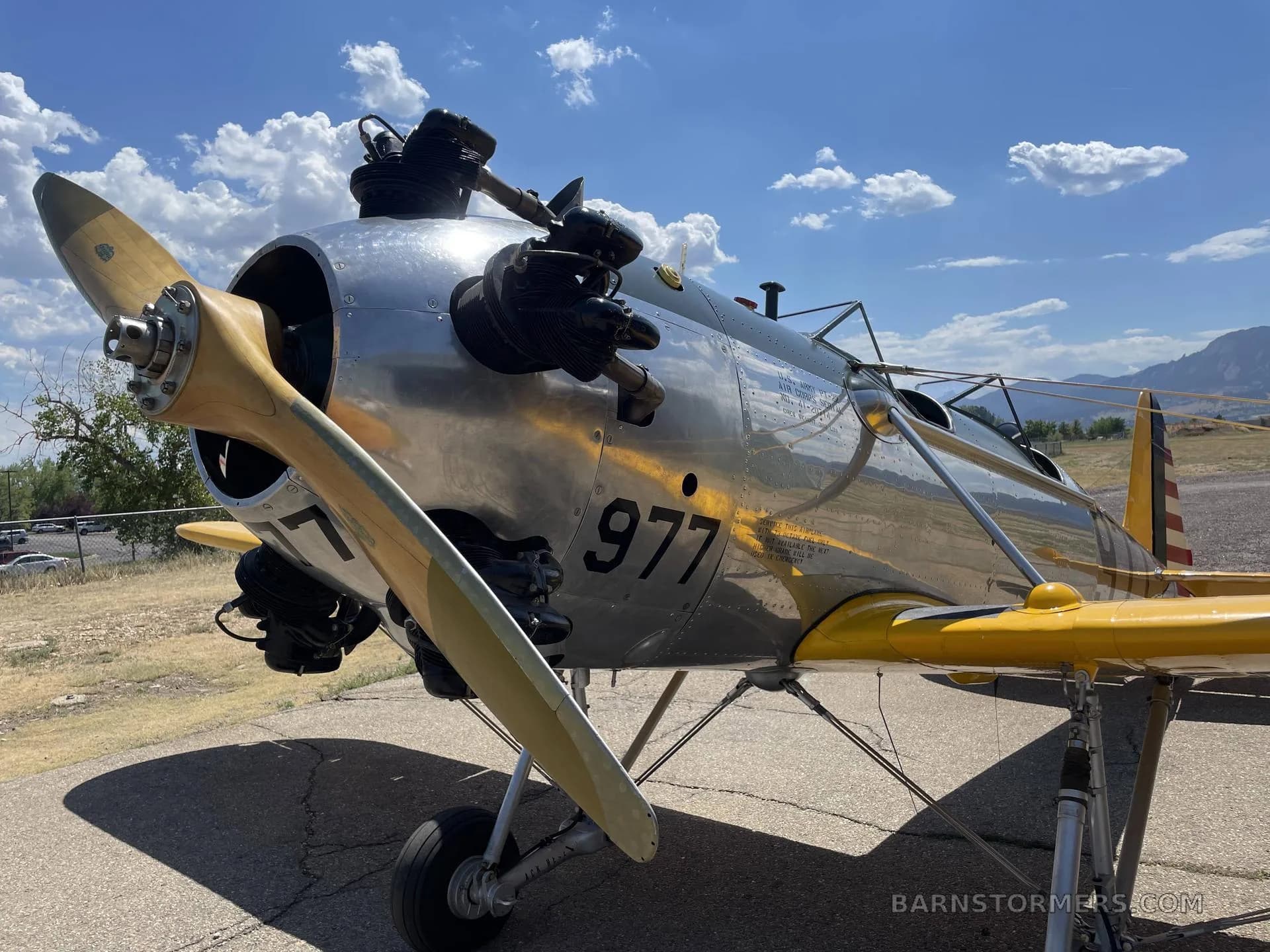 A close-up view of the front of a silver and yellow biplane, showing the propeller, engine, and '977' on the fuselage.