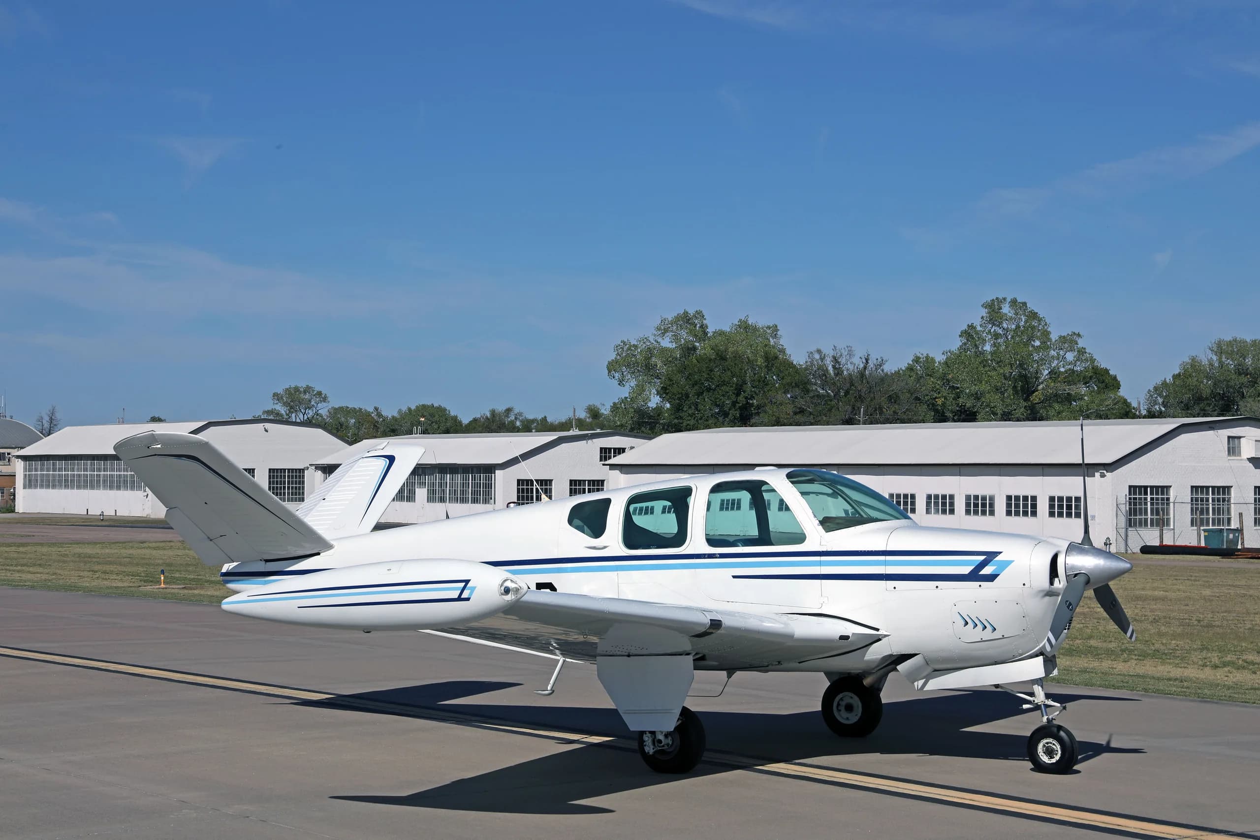 A side view of a white single-engine aircraft with blue stripes, registration N4696D, parked on an airfield.