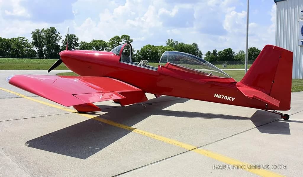 A red single-engine aircraft, registration N870KY, with its bubble canopy open, parked on an airfield.