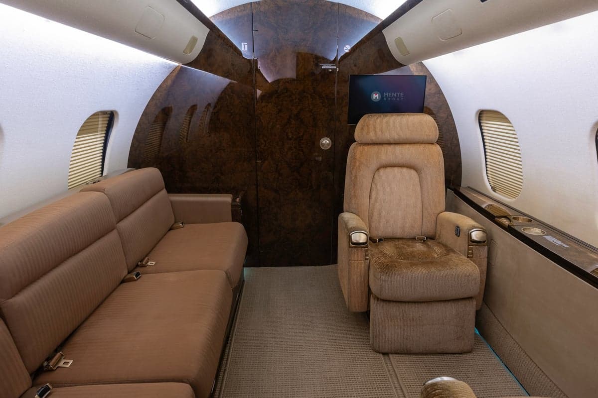 The interior of a Bombardier Global Express aircraft with tan leather seats and a couch.