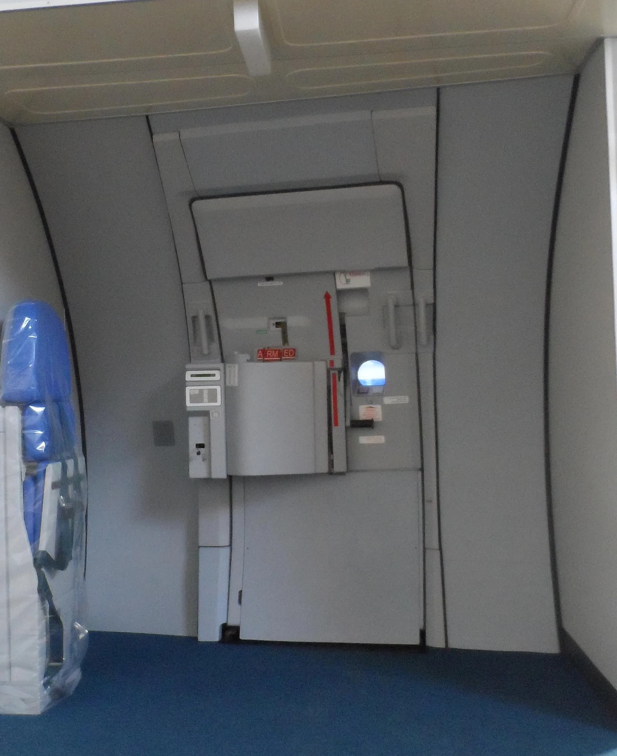 An aircraft cabin door with a wrapped blue seat to the left, showing the "ARMED" indicator.