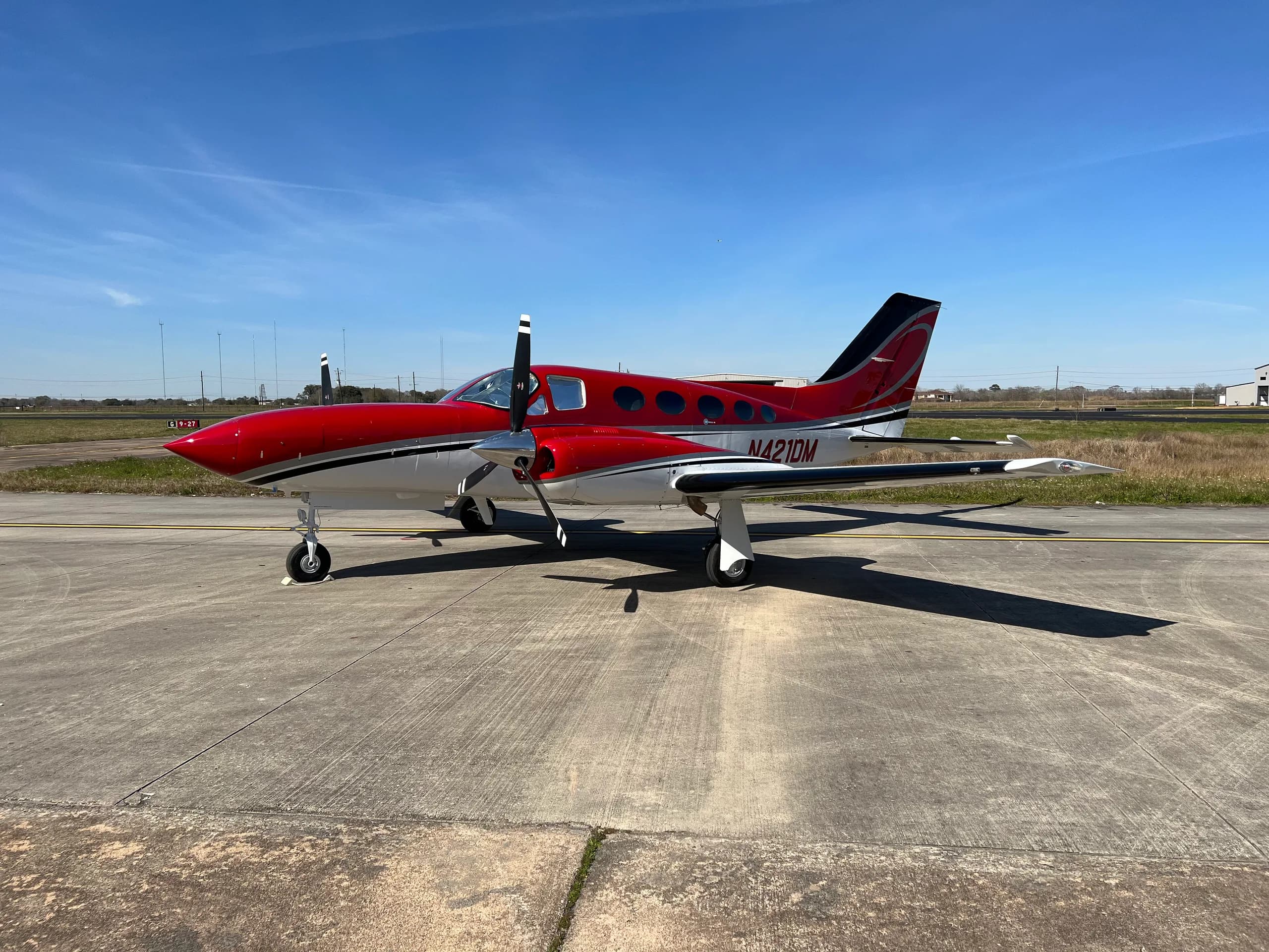A red and white twin-engine aircraft sits on the tarmac on a sunny day.