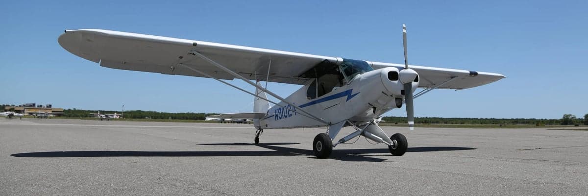 A white and blue Piper Cub on the tarmac.